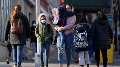 Children and their caregivers arrive for school in New York, Monday, March 7, 2022. COVID cases are starting to rise again in the United States, with numbers up in most states and up steeply in several. One expert says he expects more of a “bump” than the monstrous surge of the first omicron wave, but another says it’s unclear how high the curve will rise and it may be more like a hill.