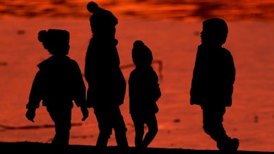 Kids are silhouetted against a pond at a park in Lenexa, Kan., on Saturday, Dec. 26, 2020.