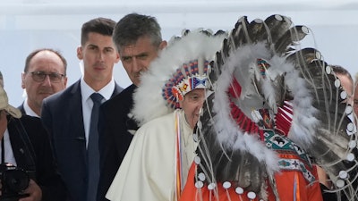 Massimiliano Strappetti, left, watches Pope Francis putting on an indigenous headdress during a meeting with indigenous communities, including First Nations, Metis and Inuit, at Our Lady of Seven Sorrows Catholic Church in Maskwacis, Canada, Monday, July 25, 2022. Francis has promoted the Vatican nurse whom he credited with saving his life to be his 'personal health care assistant.' The Vatican announced the appointment of Massimiliano Strappetti, currently the nursing coordinator of the Vatican's health department, in a one-line statement Thursday, Aug. 4, 2022.