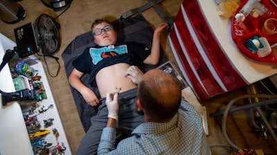 Nathan Hill cleans the gastrostomy tube on his son Brady, 14, at their home in Meridian, Idaho, June 19, 2023. Brady survived a rare brain cancer as a baby, but requires round the clock care.