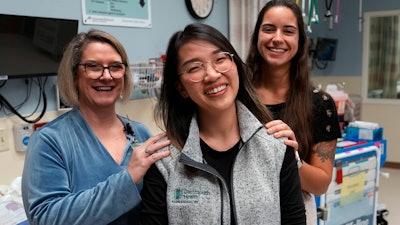 Andy Hoang, a recent nursing graduate, center, poses with co-workers Lisa Davenport, left, and Justina Terino at the spot where she was stricken recently during a cardiac training session at the Dartmouth-Hitchcock Medical Center, Tuesday, Dec. 5, 2023, in Lebanon, N.H.