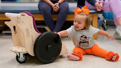 Freya Baudoin, 18 months, sits in her mobility chair for the first time at the Children's Hospital New Orleans Rehabilitation Center in Metairie, La., Monday, Oct. 30, 2023. Tulane science and engineering students are making the second batch of mobility chairs for toddlers, that will eventually go to pediatric patients at Children's Hospital.
