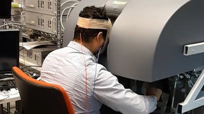 A study participant undergoing noninvasive brain stimulation sits at the surgical robot console using virtual reality simulations of needle-driving exercises.