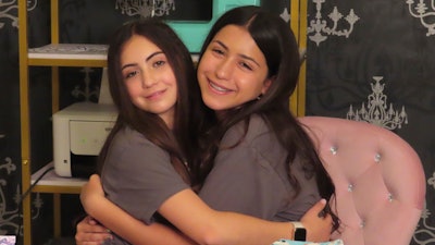 Audrina Demma, left, and her sister Giuliana hug in the basement at the sewing station of their Freehold, N.J., home on June 19, 2024. The sisters have sewn and donated 1,800 hospital gowns to sick children in 36 states plus Africa. Giuliana was inspired by seeing her baby cousin wearing an ugly, ill-fitting gown while hospitalized with brain cancer in 2017.