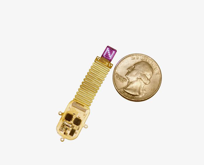 The thin, flexible, wireless device sits next to a quarter for scale. Device emits complex patterns of light (shown here as an 'N') to transmit information directly to the brain.