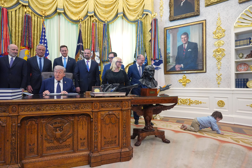 Travis Smith, 2, crawls on the floor as President Donald Trump speaks during an event on health care affordability in the Oval Office at the White House, Thursday, April 23, 2026, in Washington.