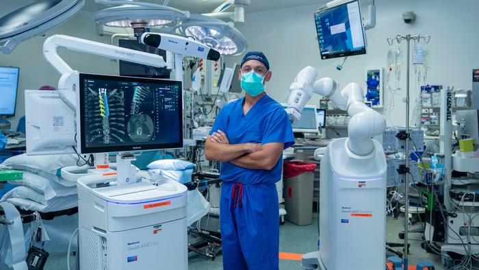 Joseph Osorio, MD, PhD, neurosurgeon at San Diego Health, stands beside the new AI-powered robotic spine surgery system in an operating room at Jacobs Medical Center.