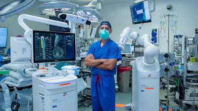 Joseph Osorio, MD, PhD, neurosurgeon at San Diego Health, stands beside the new AI-powered robotic spine surgery system in an operating room at Jacobs Medical Center.