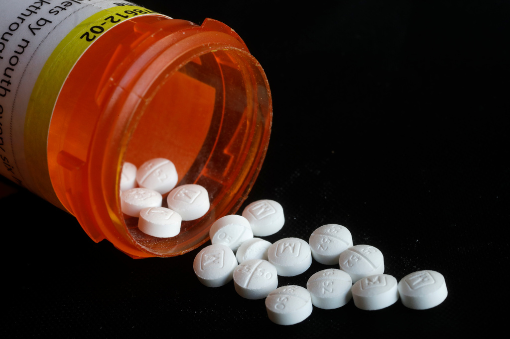 White prescription tablets spilling from an orange medication bottle against a black background