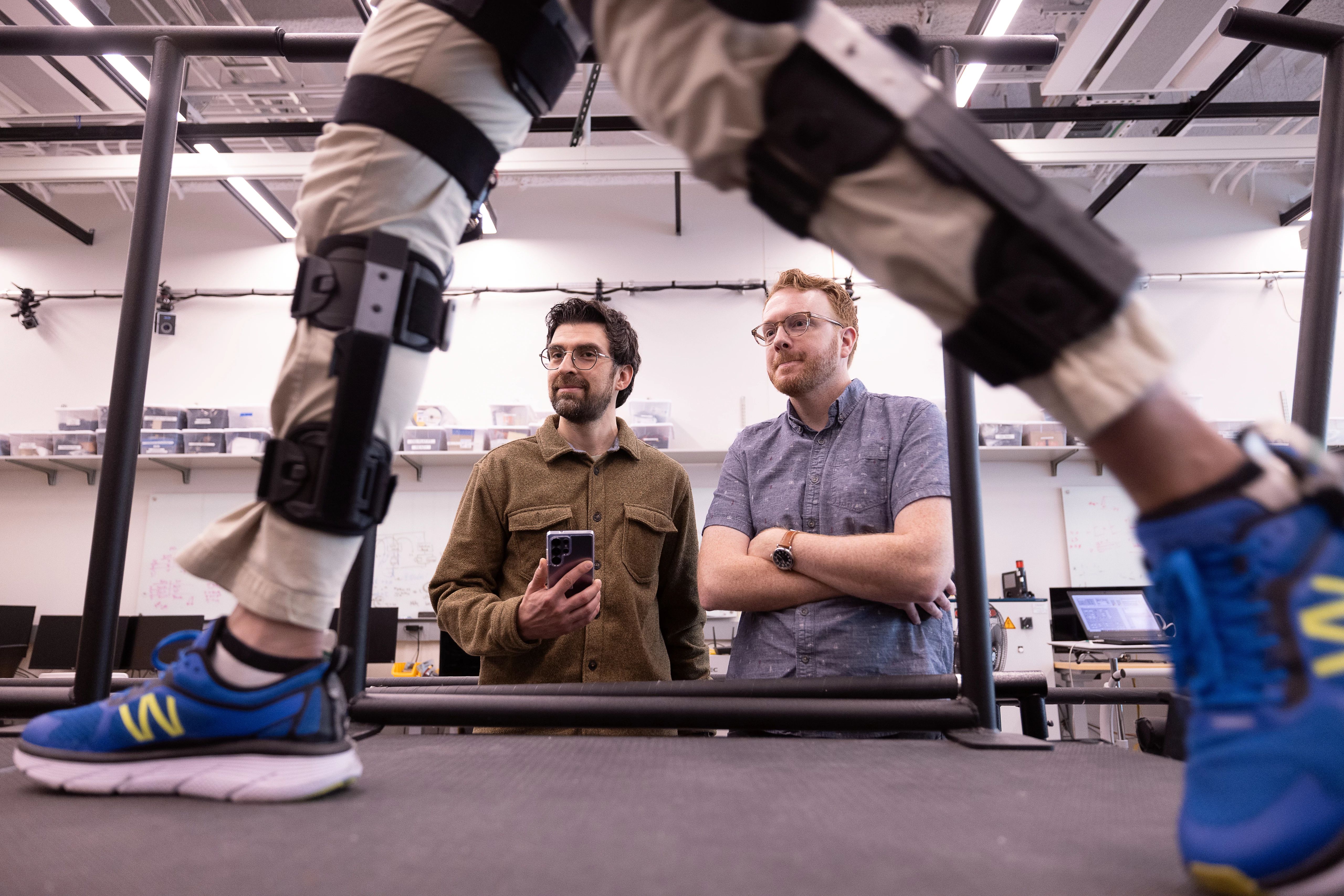 Nikhil Divekar, a postdoctoral research fellow in the Locomotor Control Systems Laboratory, demonstrates the knee exoskeleton on raised platform in the lab while fellow postdoc Ernesto Hernandez Hinojosa and professor Robert Gregg observe.