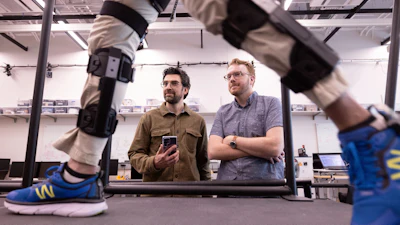 Nikhil Divekar, a postdoctoral research fellow in the Locomotor Control Systems Laboratory, demonstrates the knee exoskeleton on raised platform in the lab while fellow postdoc Ernesto Hernandez Hinojosa and professor Robert Gregg observe.
