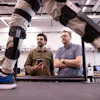 Nikhil Divekar, a postdoctoral research fellow in the Locomotor Control Systems Laboratory, demonstrates the knee exoskeleton on raised platform in the lab while fellow postdoc Ernesto Hernandez Hinojosa and professor Robert Gregg observe.