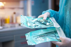 Healthcare worker in blue scrubs holding sterile surgical instrument packages in a medical facility