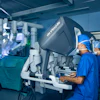 Surgeons operating da Vinci robotic surgical system in sterile operating room with monitors displaying procedure