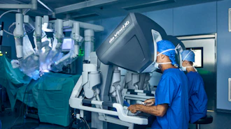 Surgeons operating da Vinci robotic surgical system in sterile operating room with monitors displaying procedure