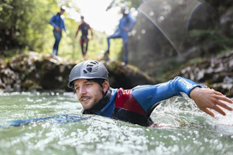 Man canyoning in turquoise river wearing helmet and blue harness with group in background