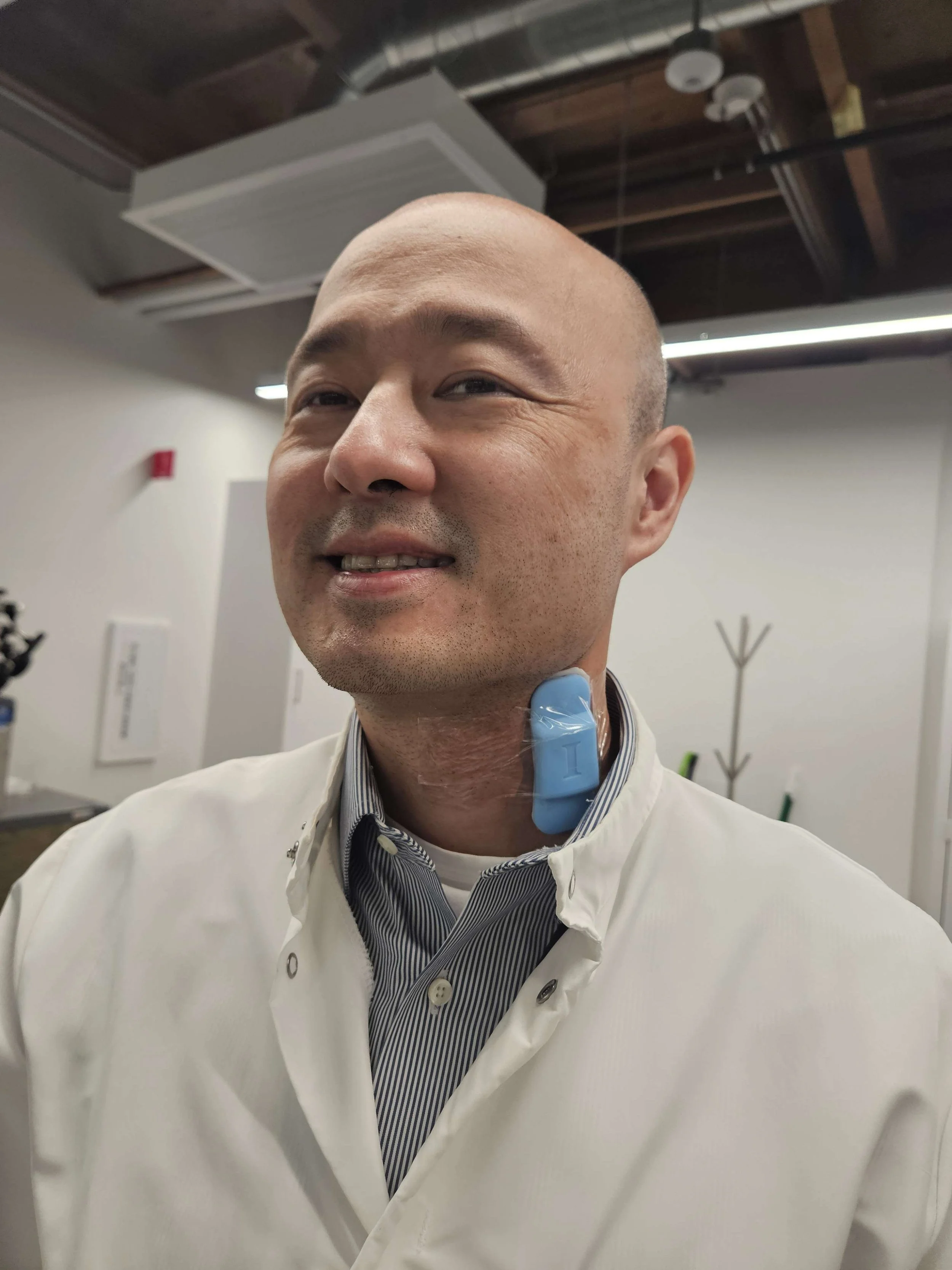 Professional man in white lab coat and striped shirt smiling in modern office environment