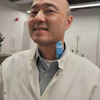 Professional man in white lab coat and striped shirt smiling in modern office environment