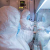 Laboratory technicians in protective suits working in a biosafety cabinet with scientific equipment