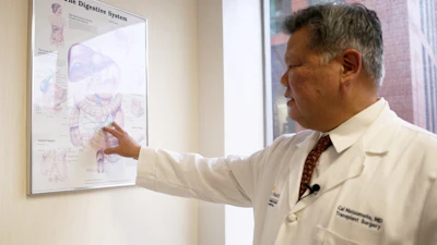 Medical professional in white coat pointing to digestive system anatomy chart during educational presentation