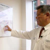 Medical professional in white coat pointing to digestive system anatomy chart during educational presentation