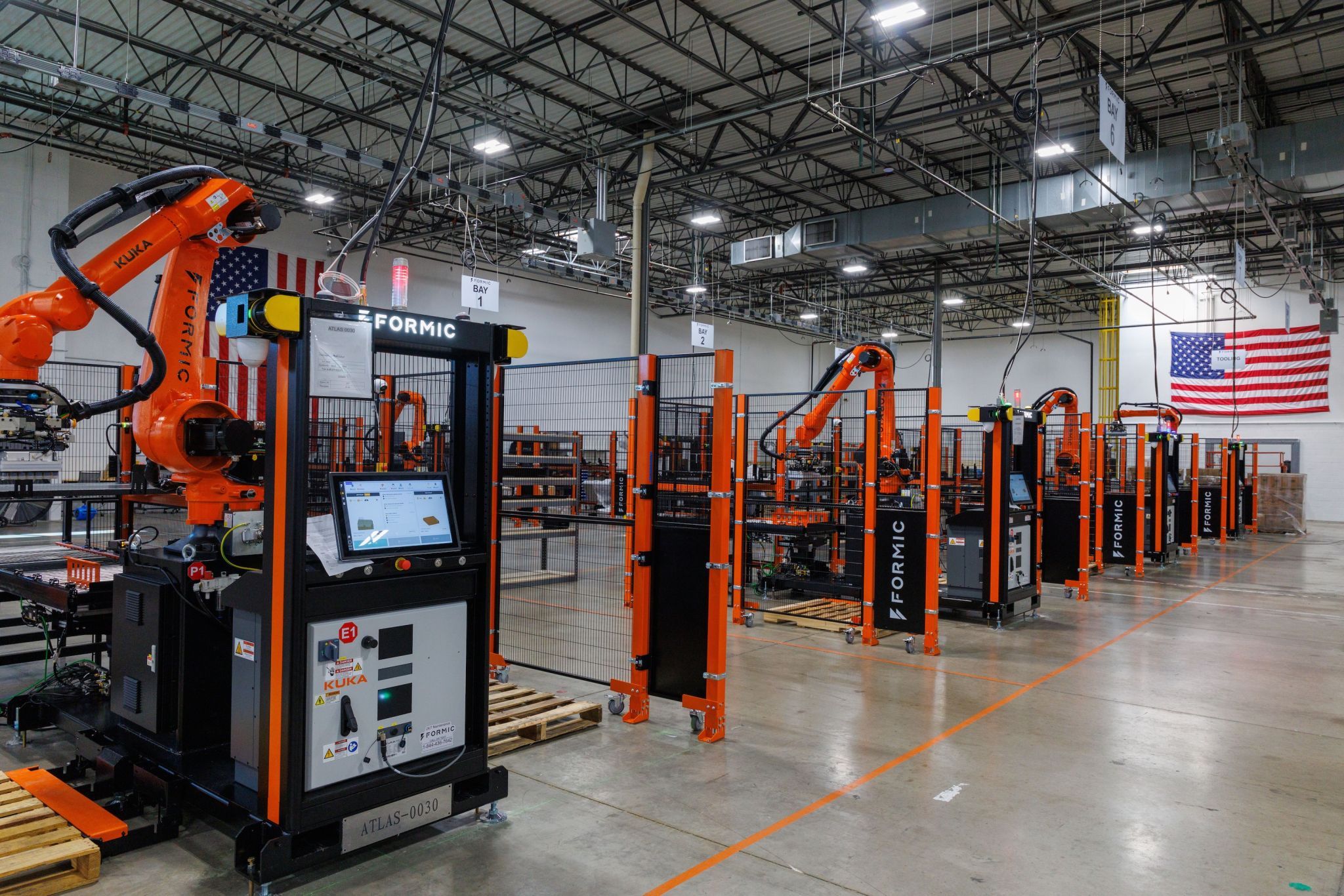 Industrial robotic welding facility with orange automation equipment and American flag in warehouse setting