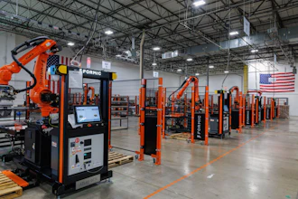 Industrial robotic welding facility with orange automation equipment and American flag in warehouse setting