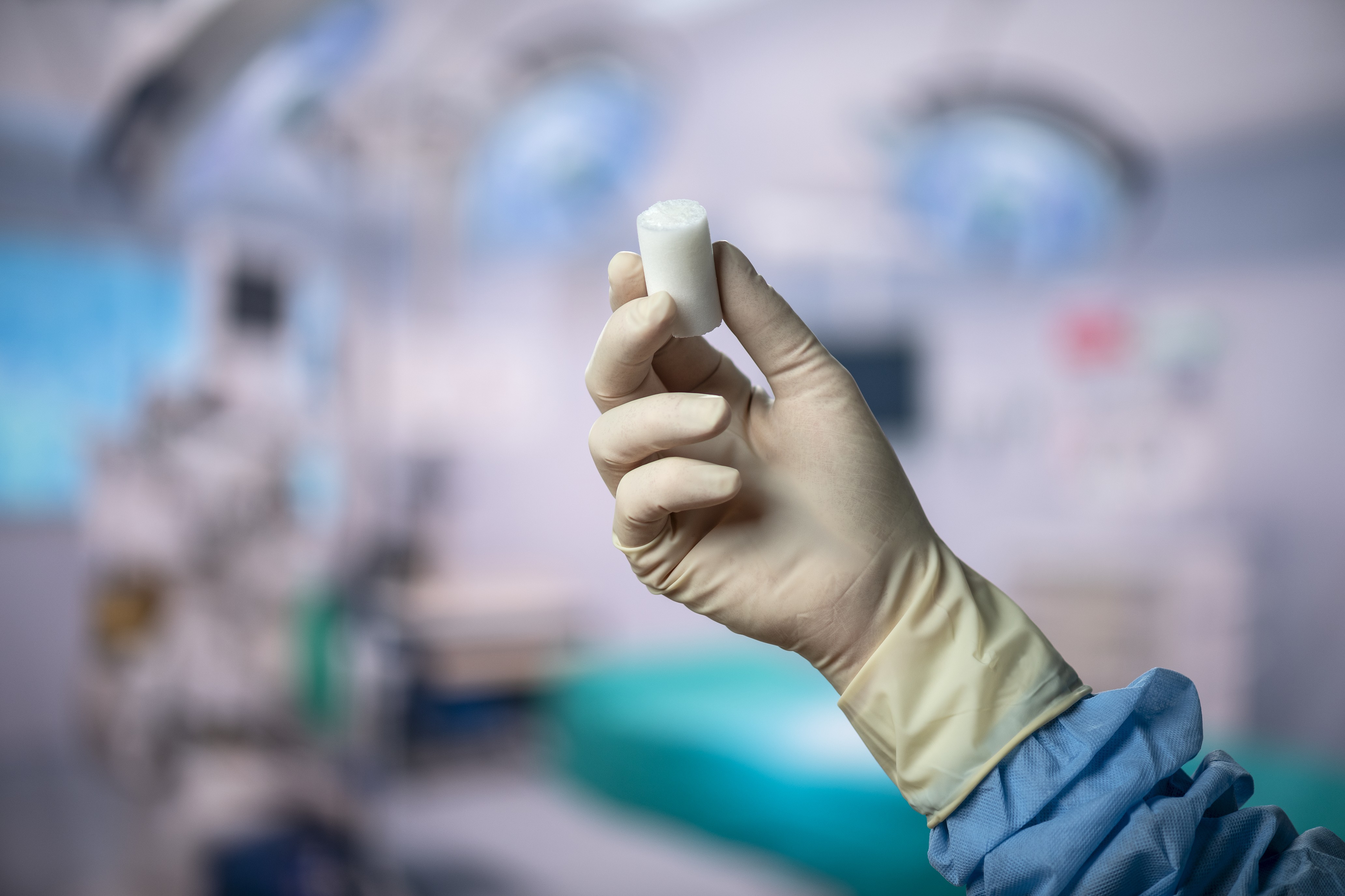 Gloved hand holding white medical inhaler device in clinical healthcare setting