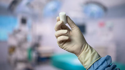 Gloved hand holding white medical inhaler device in clinical healthcare setting