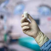 Gloved hand holding white medical inhaler device in clinical healthcare setting
