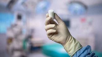 Gloved hand holding white medical inhaler device in clinical healthcare setting