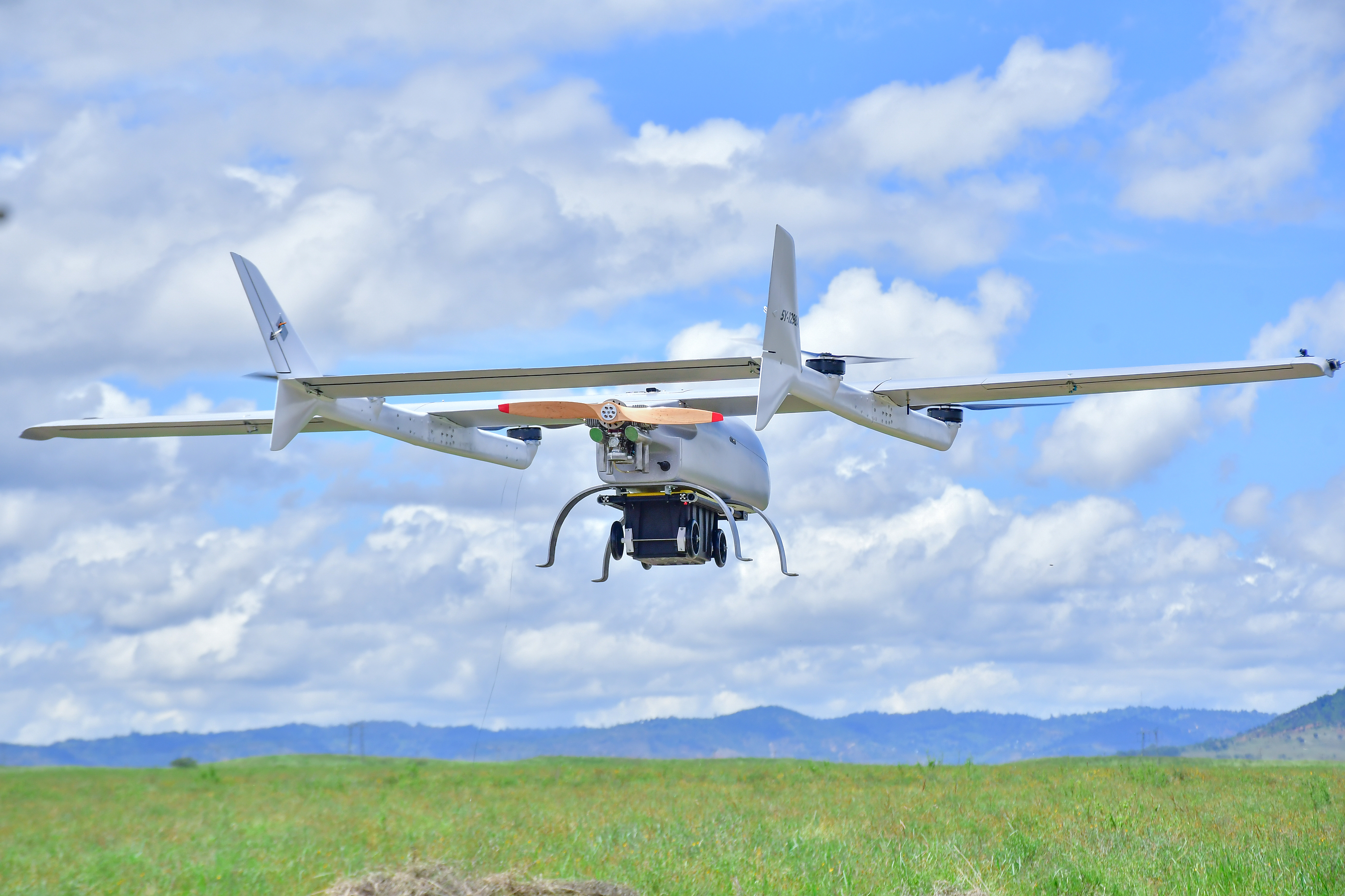 Agricultural drone flying over green field with mountains under blue sky