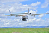 Agricultural drone flying over green field with mountains under blue sky