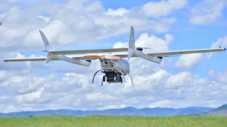 Agricultural drone flying over green field with mountains under blue sky