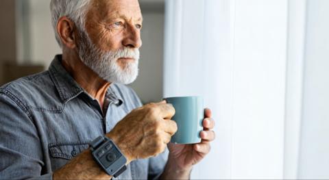 Senior man with gray beard holding a teal mug while looking out a window