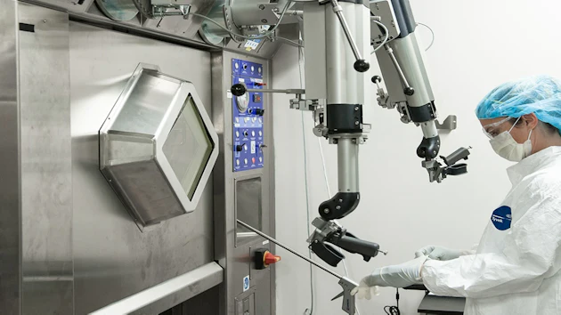 Surgeon in sterile attire operating advanced robotic surgical system with articulated arms and control interface