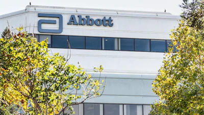 Abbott corporate building exterior with blue logo signage and windows surrounded by green foliage