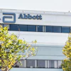 Abbott corporate building exterior with blue logo signage and windows surrounded by green foliage