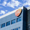GSK corporate headquarters building with orange logo sign against blue sky and clouds