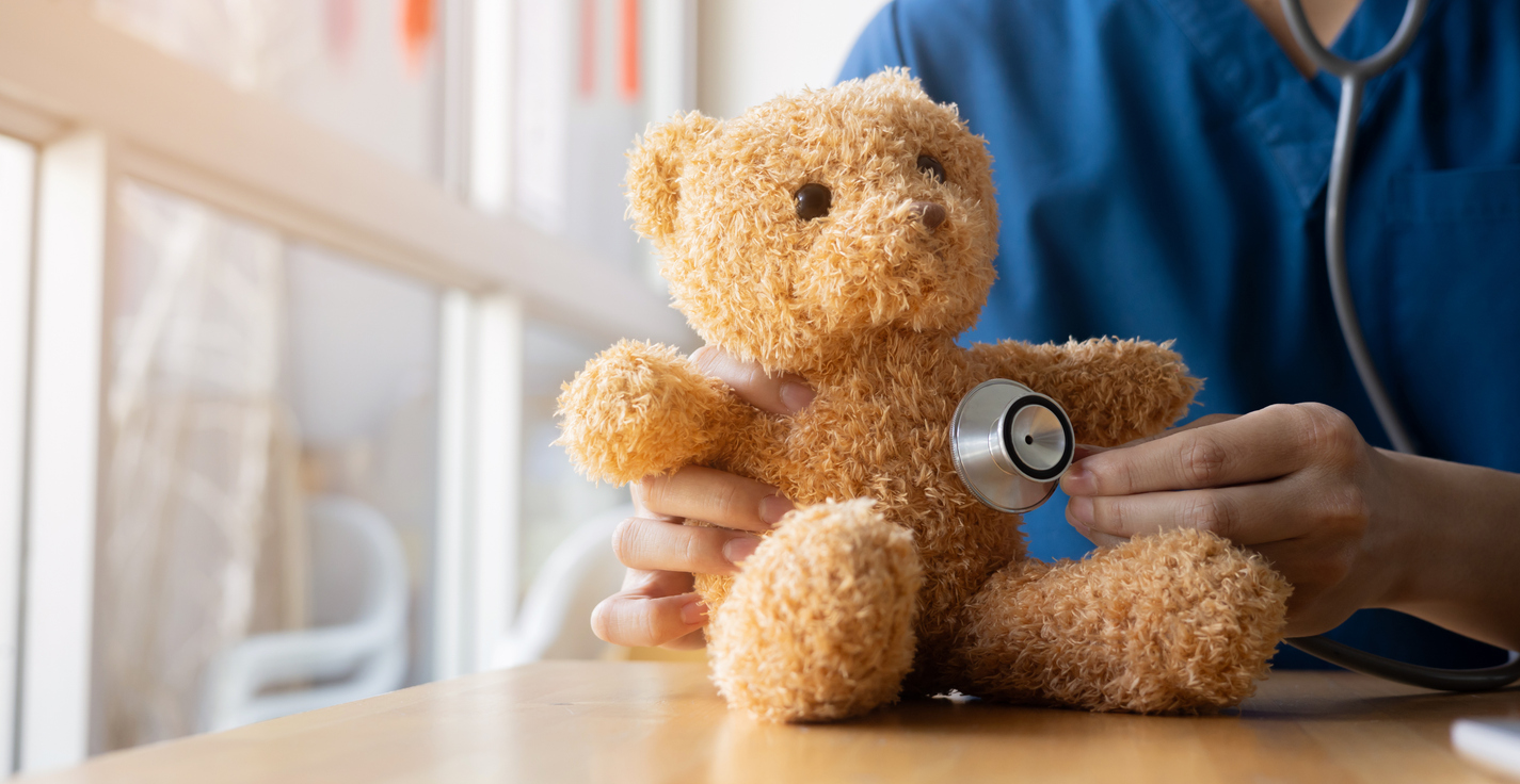 Healthcare professional using stethoscope to examine teddy bear during pediatric medical examination