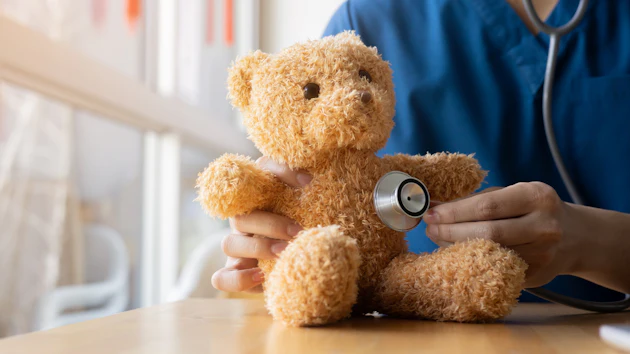 Healthcare professional using stethoscope to examine teddy bear during pediatric medical examination