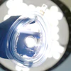 Gloved hand holding clear surgical mask under bright overhead operating room light