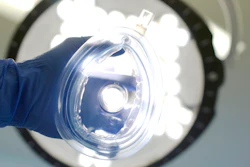 Gloved hand holding clear surgical mask under bright overhead operating room light