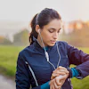 Woman jogging outdoors wearing earbuds and checking smartwatch during sunset run