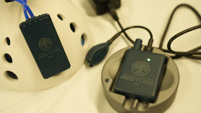 Two black Restore portable power banks with tree logo displayed on cream-colored charging dock with blue and black cables