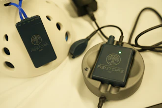 Two black Restore portable power banks with tree logo displayed on cream-colored charging dock with blue and black cables