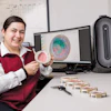 Scientist holding petri dish with bacterial culture at laboratory workstation with analysis software displayed on monitors
