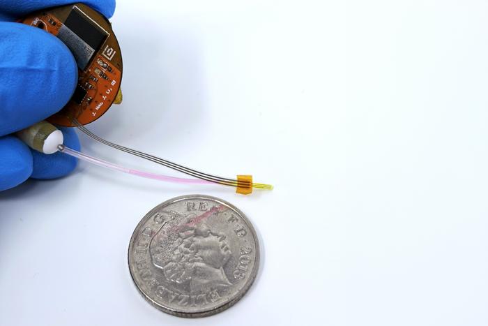 Miniature circuit board component held next to UK coin for scale comparison