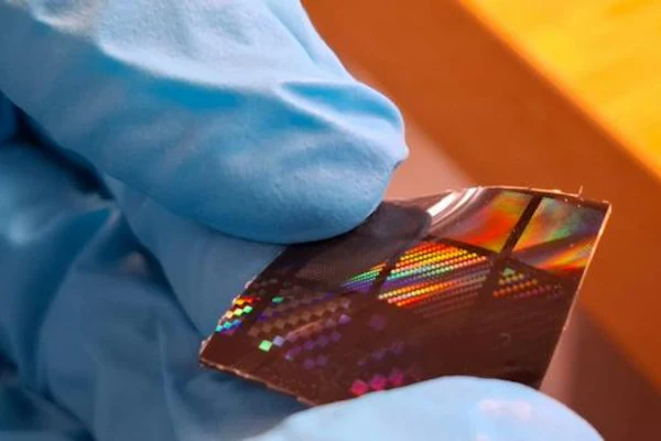 Gloved hand holding a colorful semiconductor chip with orange and yellow lighting