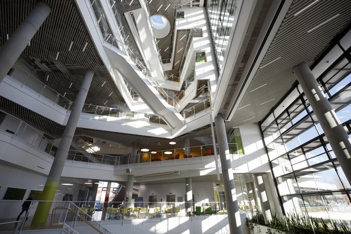 Modern spiral atrium with multiple levels, glass railings, natural skylighting, and concrete columns in contemporary building interior